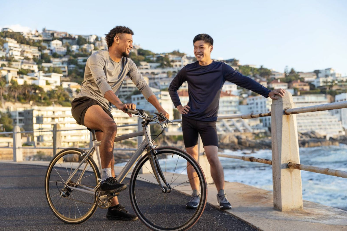 Man on a bike standing next to his friend at the beach. He is waring Bauerfeind's MalleoTrain Ankle support 