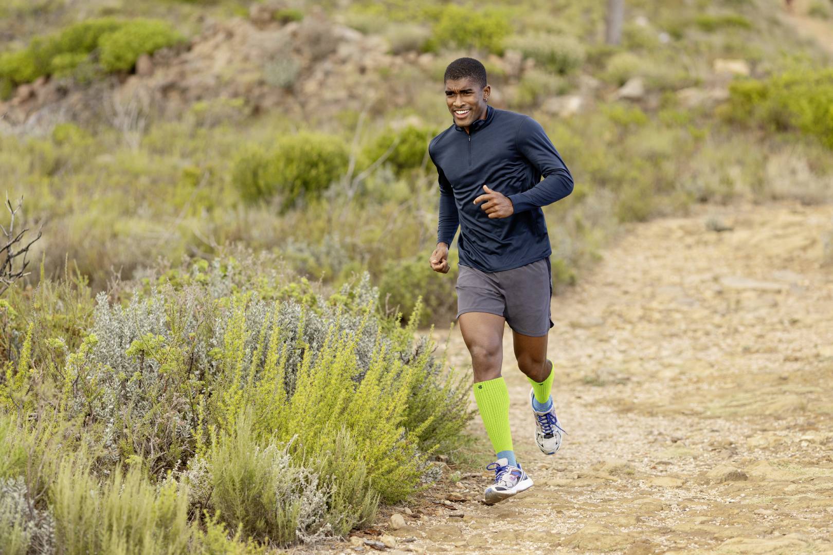 man running on a trail in performance socks. He seems to be experiencing discomfort, common to itb syndrome