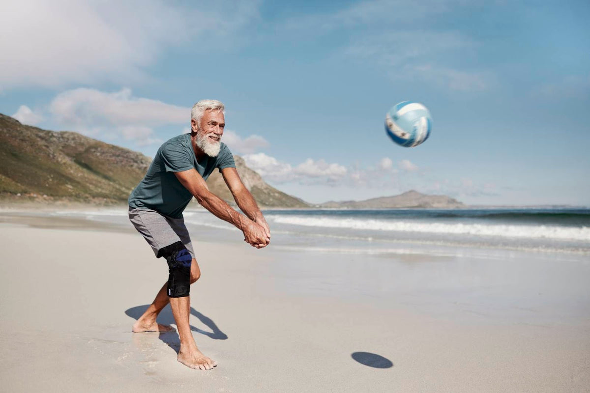 Older man playing volleyball at the beach. He is wearing Bauerfeind GenuTrain OA Knee Brace for osteoarthritis 