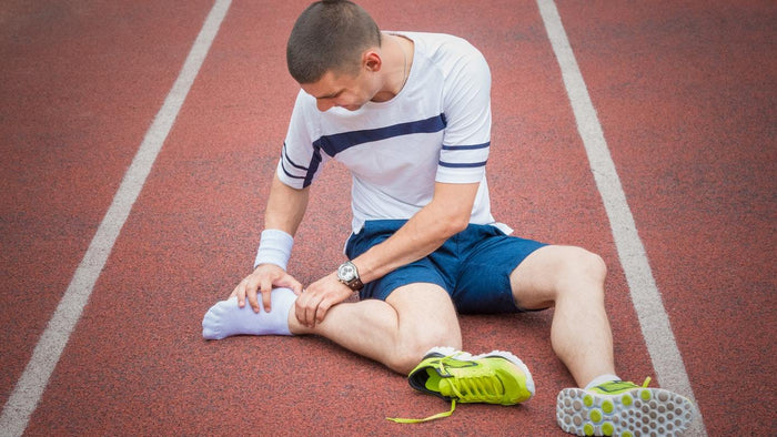 Man sitting on running track after injuring his ankle