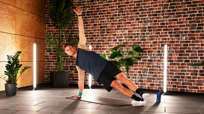 Thomas Roehler performing side planks in a studio. He is wearing Bauerfeind's Sports Wrist Strap 