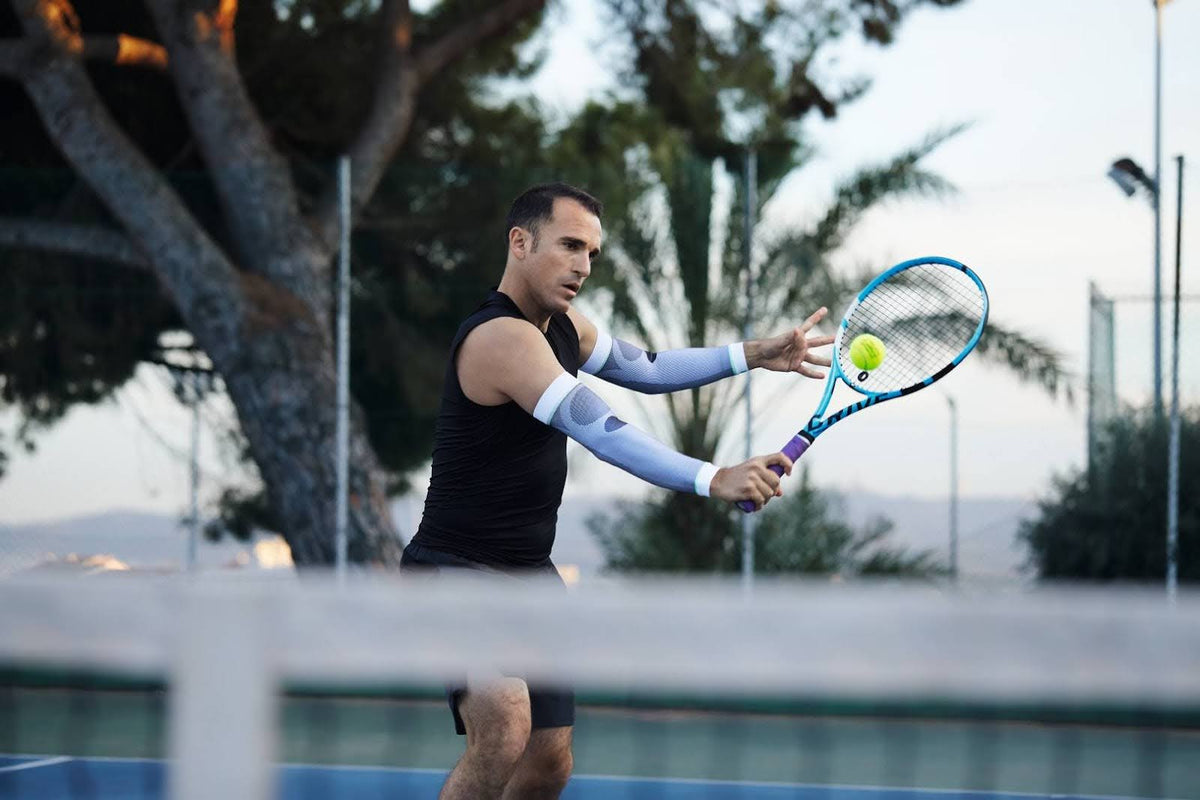 Man playing tennis, hitting a backhand shot. He is wearing Bauerfeind's Arm Compression Sleeves to support his training