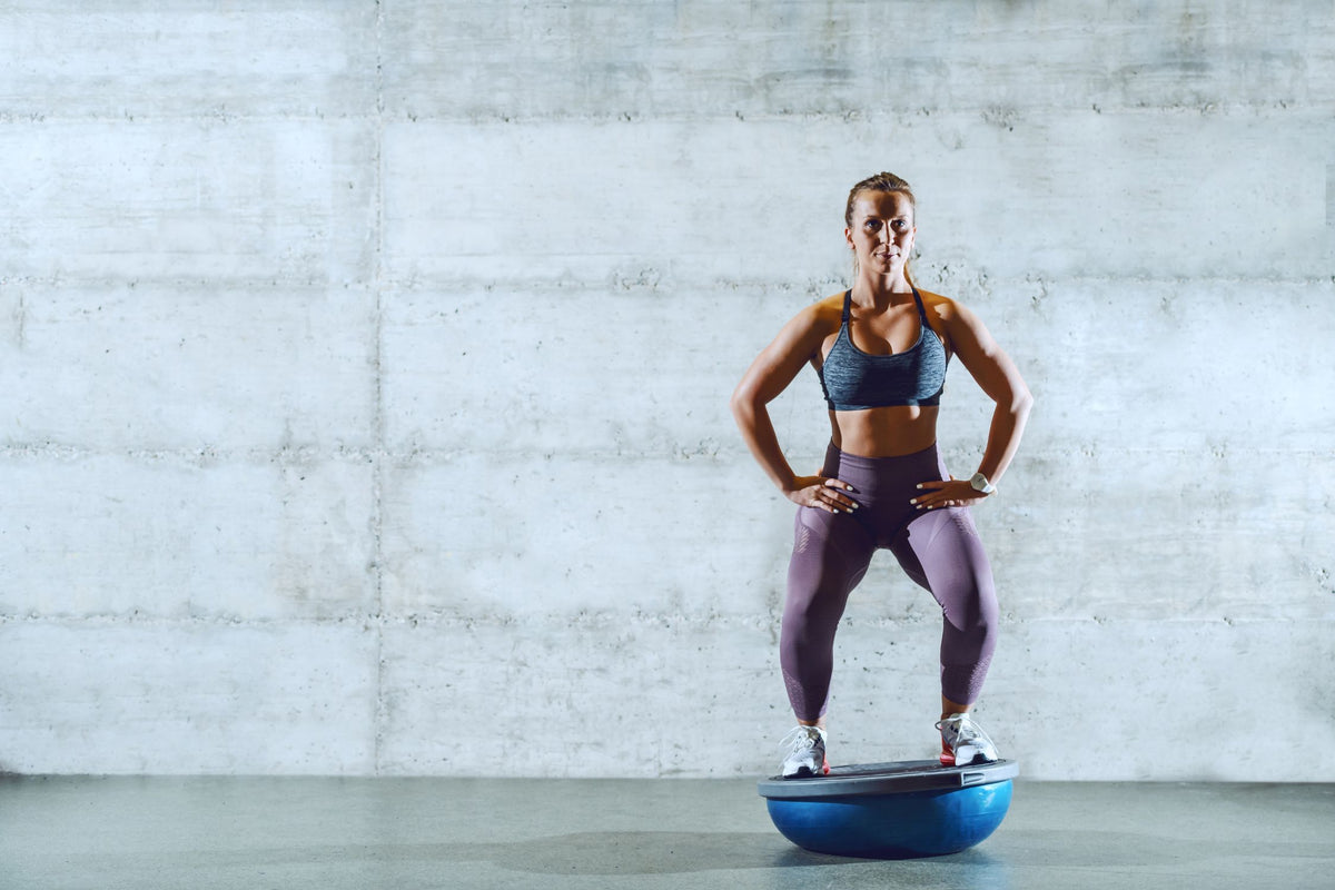 Woman performing a variation of unstable squats on a Bosu ball. She is wearing Bauerfeind's GenuTrain Knee Brace