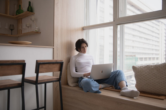 Woman sitting on a windowsill while working on her laptop, not an ideal set up to avoid back pain