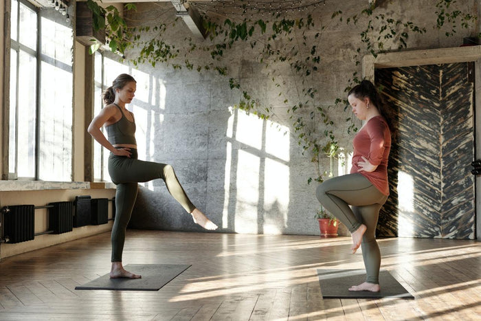 Two women doing the single leg balance: at-home strength and injury recovery exercise. Photo by Cliff Booth from Pexels