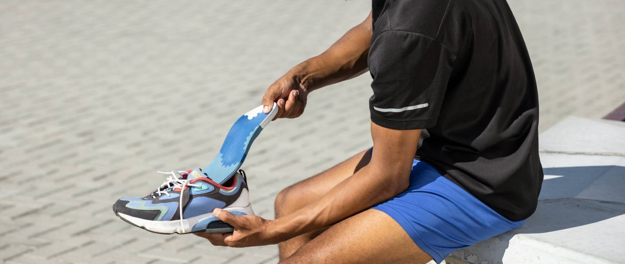 Man sitting on a bench on a sunny day. He is putting a Bauerfeind insole into his sports shoe.