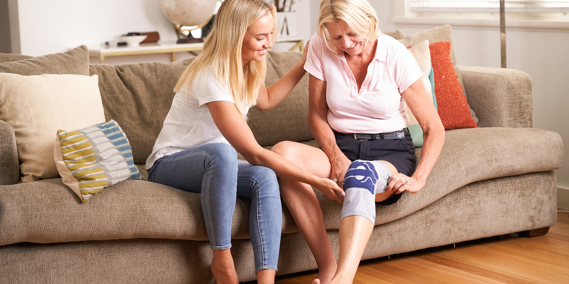 A daughter and mother sitting on the couch. The mum is wearing a Bauerfeind GenuTrain Knee Support
