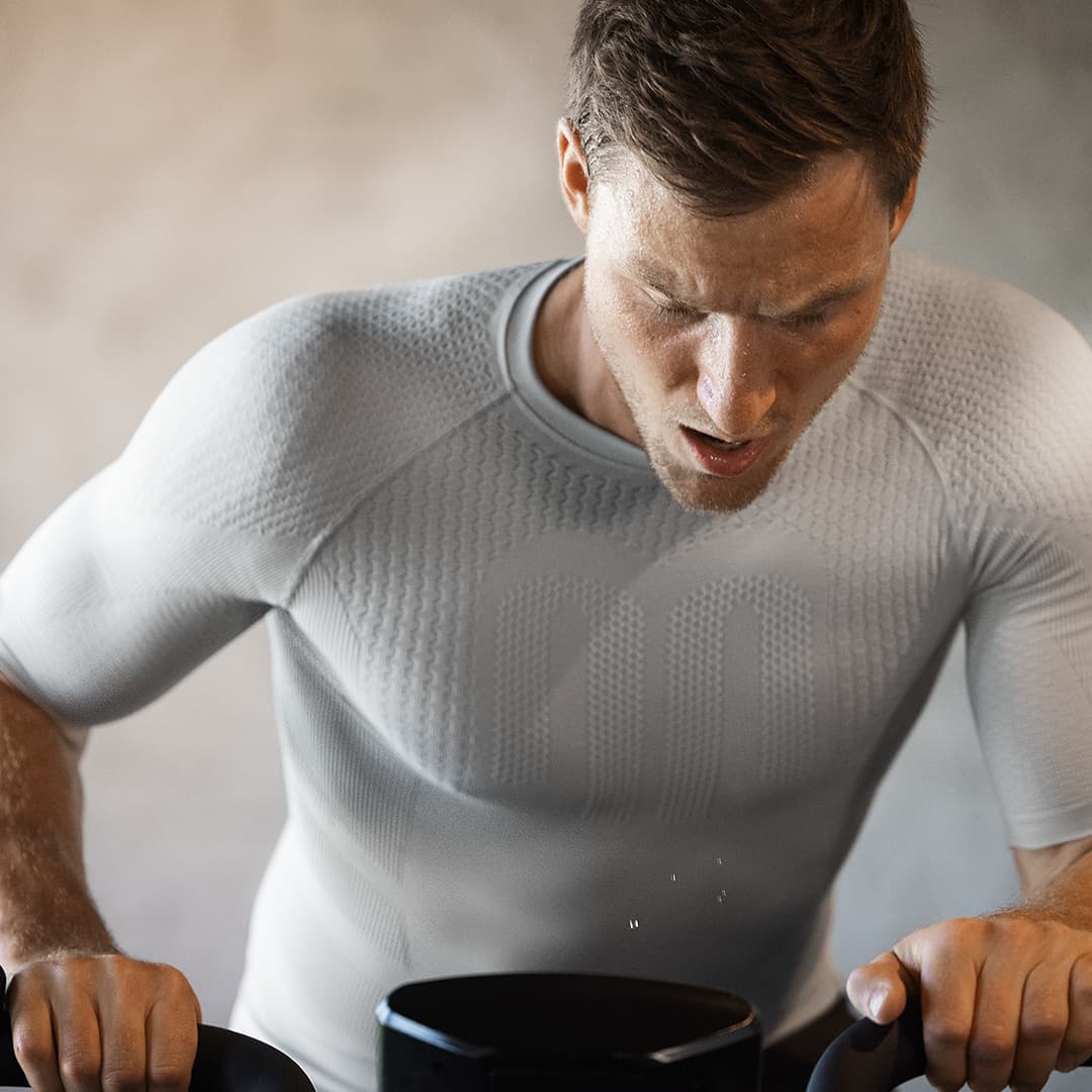 Man wearing a Bauerfeind compression shirt using a black piece of equipment against a neutral background