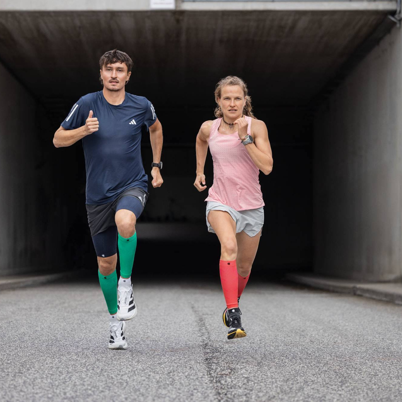Two runners, with compression sleeves, running in a tunnel.
