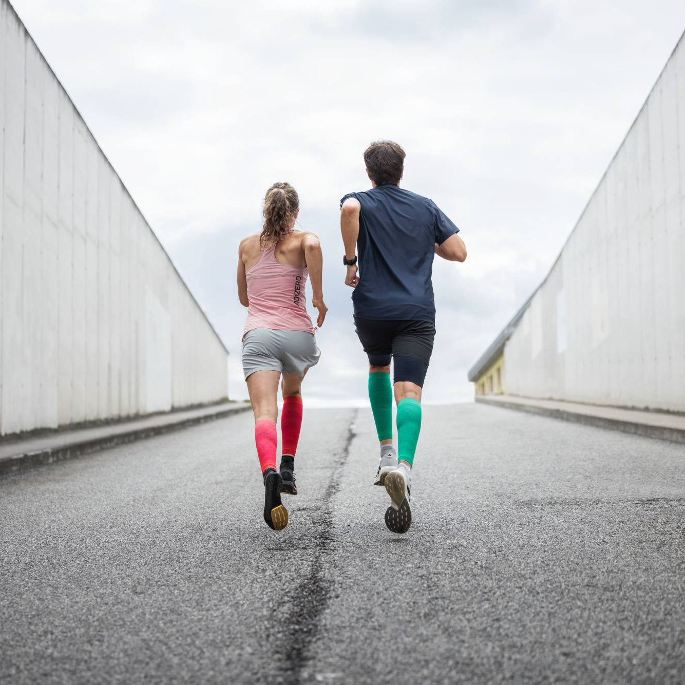 Two people running on a road with a concrete wall on either side.