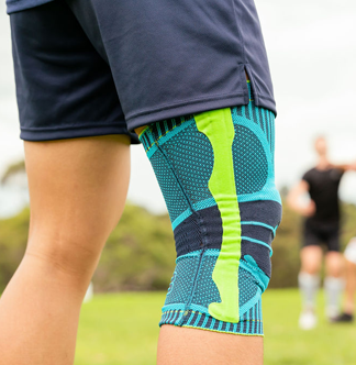 Person wearing a green and blue Bauerfeind Sports Knee Support on a grassy field.