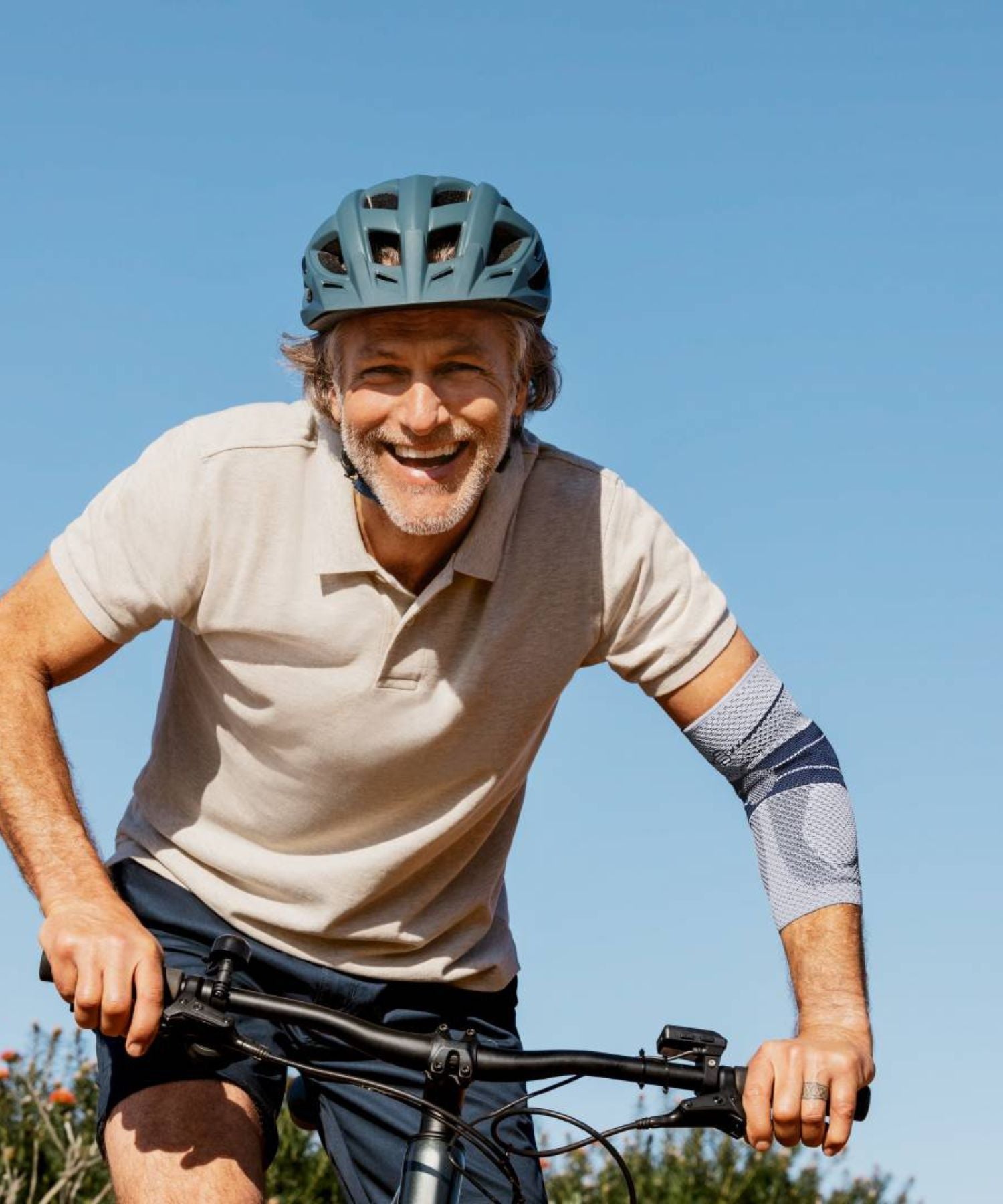 Man riding a bicycle with a clear blue sky in the background. He is wearing a Bauerfeind EpiTrain elbow support.