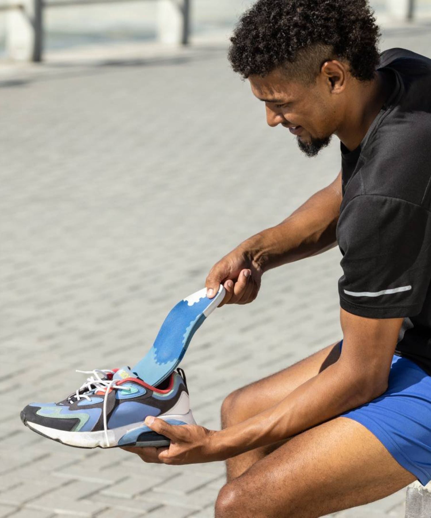Man adjusting a running shoe with a blue Bauerfeind insole on a paved surface.