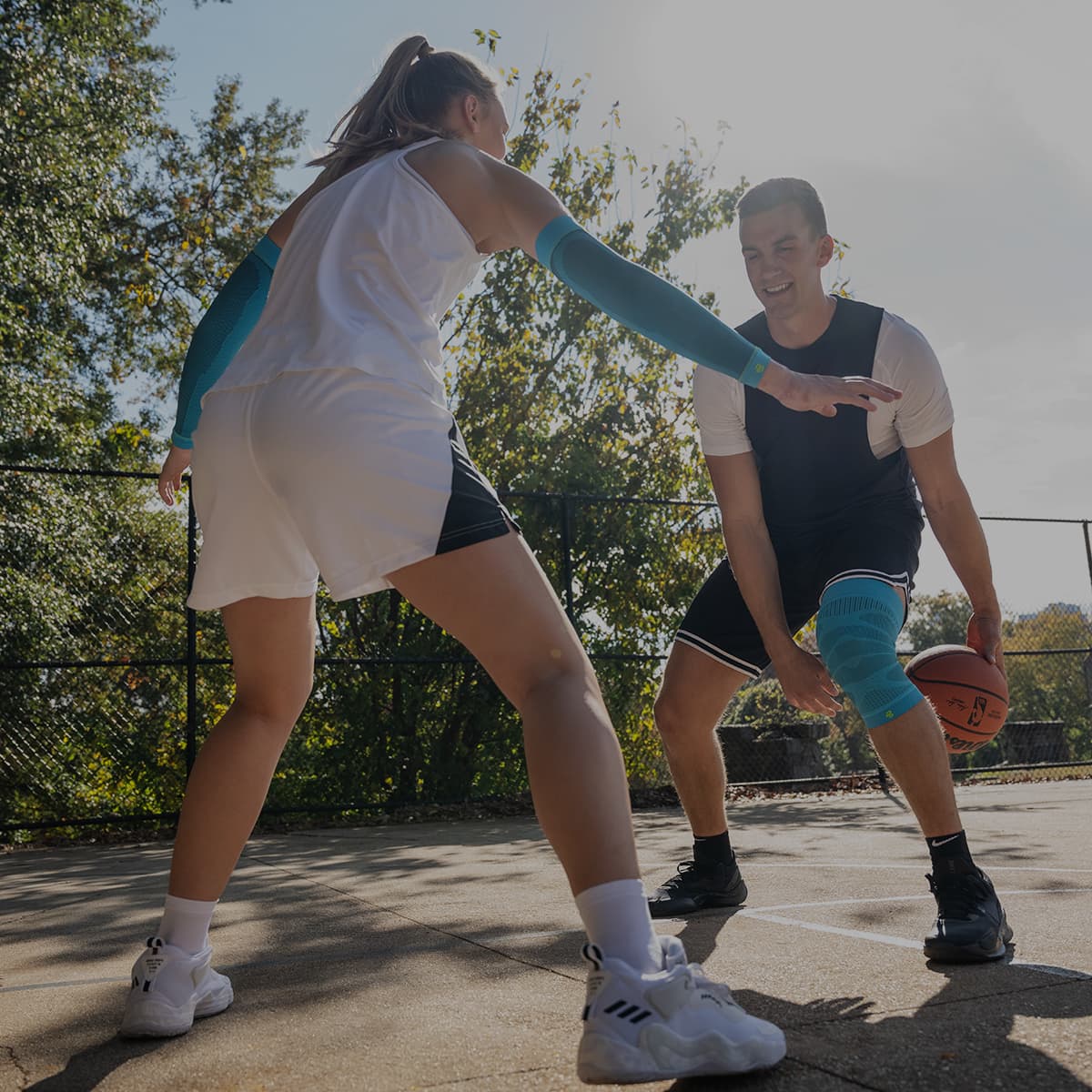 A girl and boy playing basketball, one wearing a Bauerfeind sports compression sleeve and the other wearing a Bauerfeind sports knee sleeve