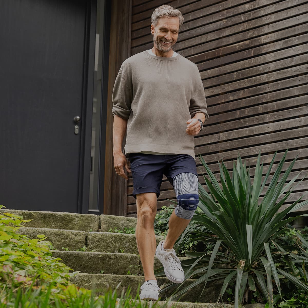 A man in front of his house wearing a Bauerfeind GenuTrain Knee Support