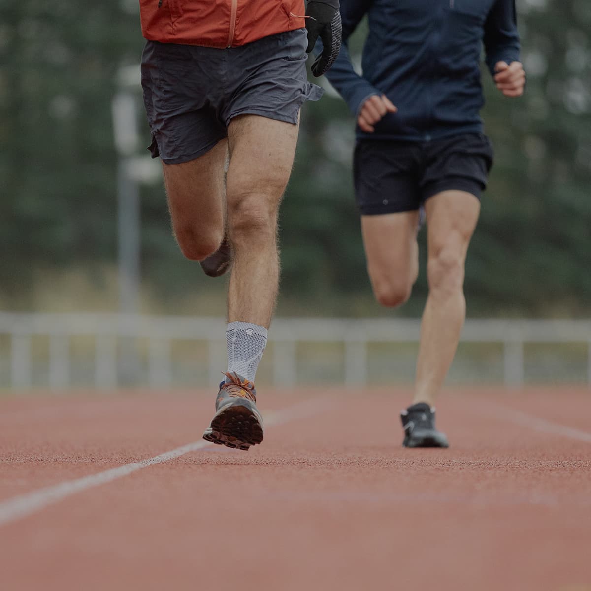 Two men running outside, one wearing a Bauerfeind MalleoTrain ankle support