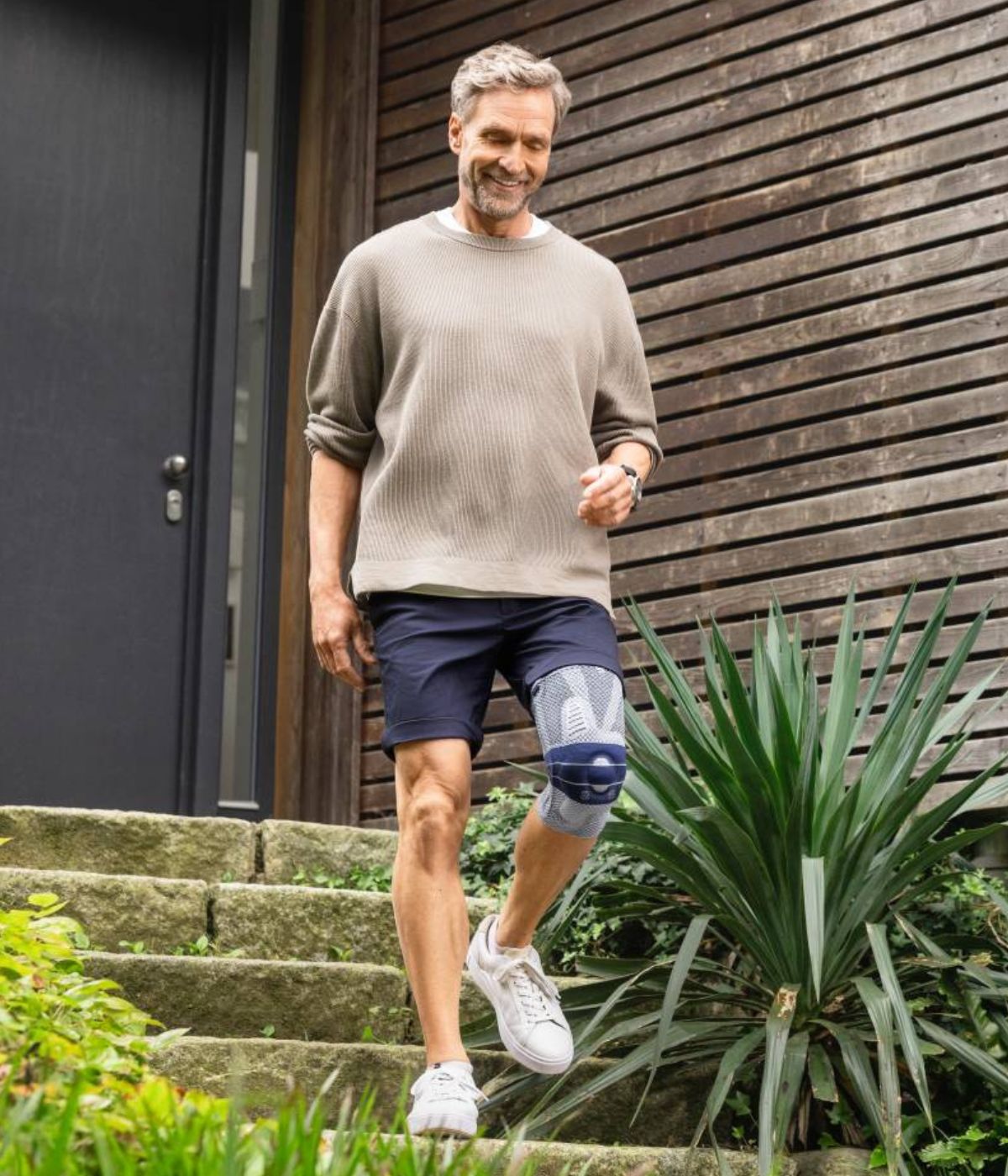 Man with a Bauerfeind GenuTrain A3 knee support walking down steps in front of a house.