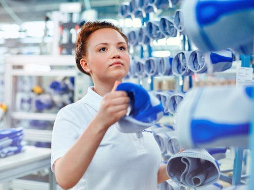 Woman racking some Bauerfeind supports from the medical range. The Supports are light grey knit with some dark blue over key areas. She looks to be in a factory, where the braces are produced.